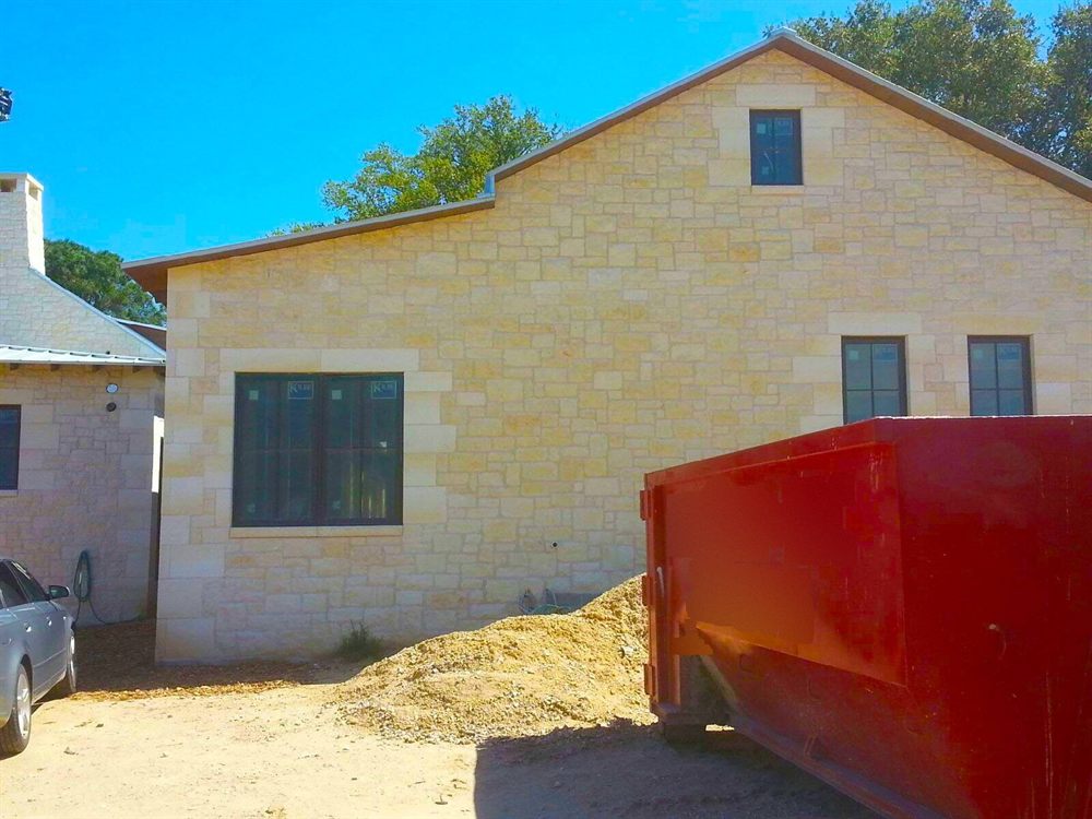 Red roll-off dumpster beside a stone home